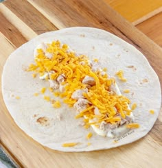 a tortilla with cheese and meat on it sitting on a wooden cutting board