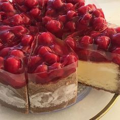 a cheesecake covered in cherries on top of a glass cake plate with one slice cut out