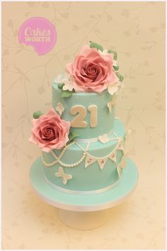 there is a blue cake with pink flowers on the top and two roses on the bottom