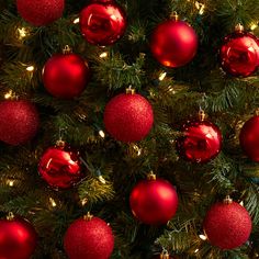 red christmas ornaments hanging from the top of a tree with gold and white lights on it