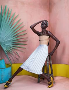 a woman in a white and tan dress standing on a stool next to a palm tree