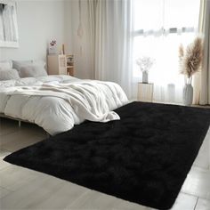 a black rug on the floor in a white room with a large bed and windows