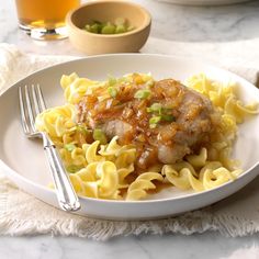 a white plate topped with pasta and meat covered in sauce next to a glass of orange juice