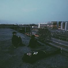 two people sitting on the ground in front of some buildings at night with their eyes closed