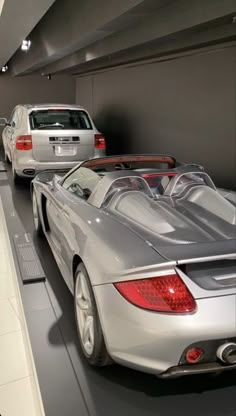 two silver sports cars are on display in a showroom with other vehicles behind them