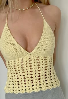 a woman wearing a yellow crochet top and grey pants with her hands on her hips