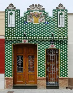 two wooden doors are open in front of a green and white building with ornate designs