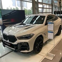 a white bmw suv is on display in a showroom with other cars behind it