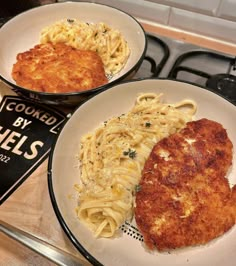 two white plates topped with pasta and meat next to a cookbook on a stove