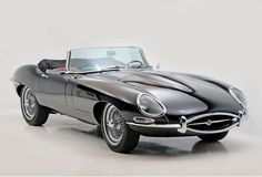 an old black sports car is parked on the floor in front of a white wall