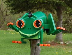 a green frog mailbox sitting on top of a wooden post