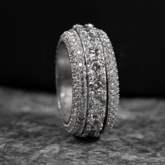 a wedding ring with three rows of diamonds on it's sides, sitting on top of a rock