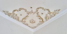 the corner of a white ceiling with gold designs on it