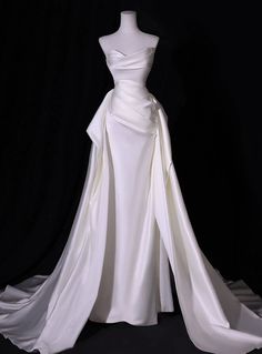 a white wedding dress on display in front of a black background with the skirt pulled back