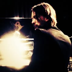 a man with long hair sitting in front of a piano