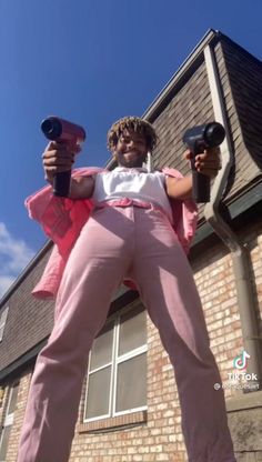 a woman in pink pants and white shirt holding two black hairdryers while standing next to a brick building