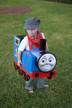 a small child in a thomas the tank engine costume is standing on some grass and holding a toy train