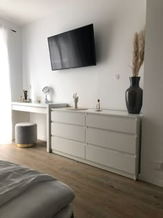 a flat screen tv mounted to the side of a wall above a white dresser in a bedroom