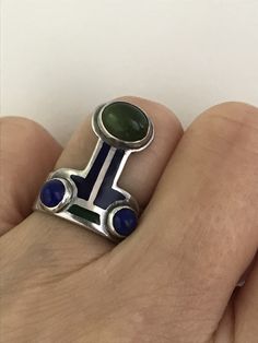 "There is a hint of arts and crafts, as well as, modernist in this unusual ring which you can wear with the Peridot facing up or down! The beautiful green stone, as well as the smaller vibrant blue Lapis are all cabochon and bezel set. The enamel is in wonderful condition. Aside from some slight wear, the ring is in overall fabulous shape. The band is almost 1/4\" wide, it is marked Sterling and has the initials CHM scratched on the silver behind the Peridot. Please see all photos for details, a Green Cabochon Enamel Jewelry, Green Enamel Jewelry With Gemstones, Modern Green Multi-stone Jewelry, Green Oval Enamel Ring With Gemstone, Oval Green Enamel Ring With Gemstone, Modern Green Cabochon Jewelry, Modern Green Collectible Jewelry, Green Cabochon Rings In Art Deco Style, Unique Green Sterling Silver Opal Ring