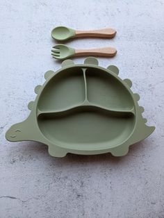 a green dinosaur shaped plate with spoons and fork