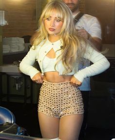 a woman with long blonde hair wearing short shorts and a crop top is posing for the camera