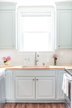 a kitchen with white cabinets and wood floors in front of a window above the sink