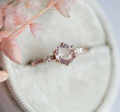 a pink diamond ring sitting on top of a white cushion