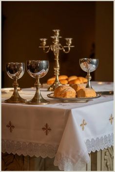 Communion table set with silver goblets, a candelabrum, and a plate of bread rolls.