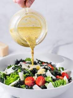 someone pouring dressing into a salad with lettuce, tomatoes and cheese on top