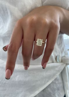 a woman's hand with a diamond ring on her left finger, wearing a white shirt