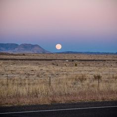 the full moon is setting over an open field