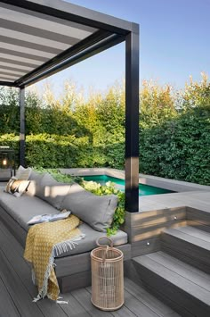 an outdoor living area with couches, pillows and plants on the deck next to a swimming pool