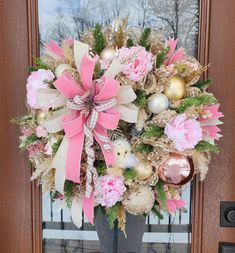 a wreath with pink flowers and gold ornaments on the front door to a house that is decorated for christmas