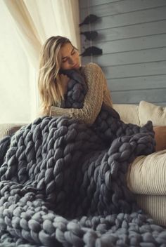 a woman laying on a bed covered in a giant chunky blanket and covering her face