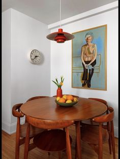 a bowl of fruit sits on a table in front of an art piece and clock