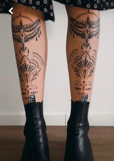 the legs and ankles of a woman with tattoos on her body, wearing black boots