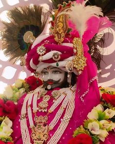 a man dressed in an elaborate costume with feathers on his head and face is surrounded by flowers