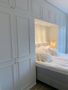 a bed with white linens and pillows in a room that has built - in cabinets