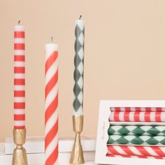 three different colored candles sitting next to each other in front of a white frame and pink wall