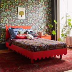 a bedroom with a red bed frame and colorful wallpaper, along with an orange rug