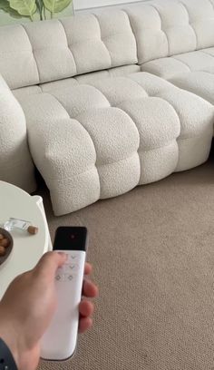 a person holding a remote control in front of a couch with a bowl of nuts on it