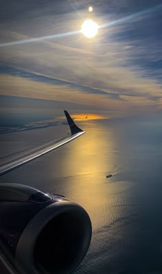 an airplane wing flying over the ocean at sunset