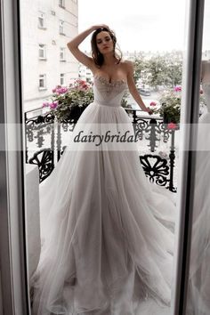 a woman standing in front of a window wearing a wedding dress and holding her hand on her head