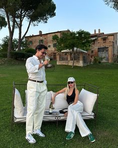 a man and woman sitting on top of a white couch in the middle of a field