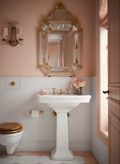 a white toilet sitting next to a sink in a bathroom under a gold framed mirror