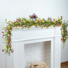 a white fireplace with flowers and greenery on top