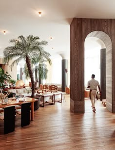 a man walking through an open living room with palm trees in the backgroud