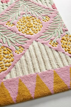 a pink rug with yellow and green designs on it, sitting on a white surface