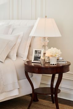 a bedroom with white bedding and a lamp on the end table next to it