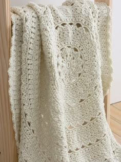 a white crocheted blanket hanging on a wooden rail with wood slats in the background